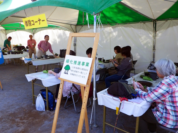 テントの下で約１4人ぐらいの受講生が寄せ植えの仕方を聞いている画像