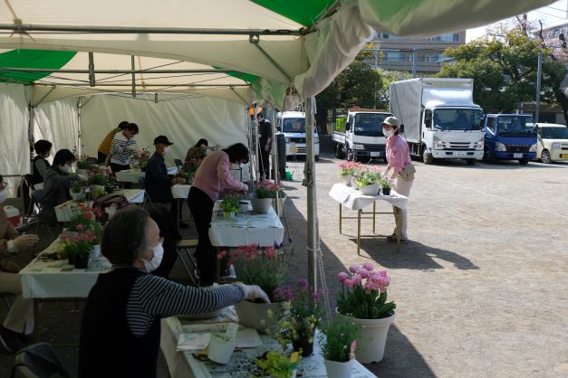 テントの下で約１2人ぐらいの受講生が寄せ植えの仕方を聞いている画像