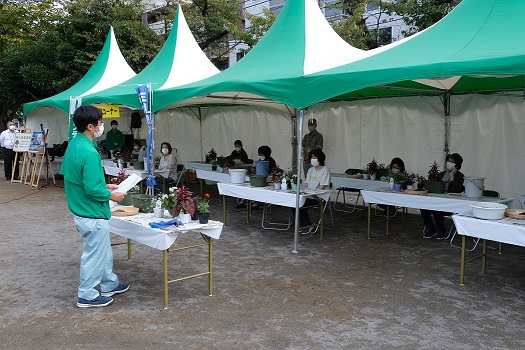 テントの下で約１2人ぐらいの受講生が寄せ植えの仕方を聞いている画像