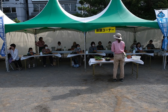 テントの下で約１4人ぐらいの受講生が寄せ植えの仕方を聞いている画像