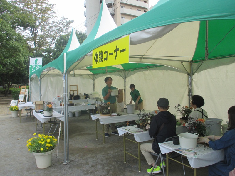 テントの下で約１4人ぐらいの受講生が寄せ植えの仕方を聞いている画像