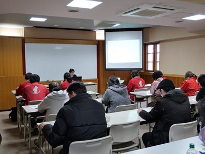 部屋の中に約２０人が講師の話を聞いている画像